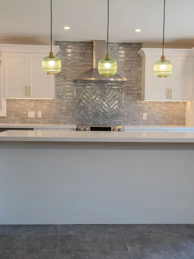 Modern kitchen with white cabinetry, gray backsplash, and green pendant lights.